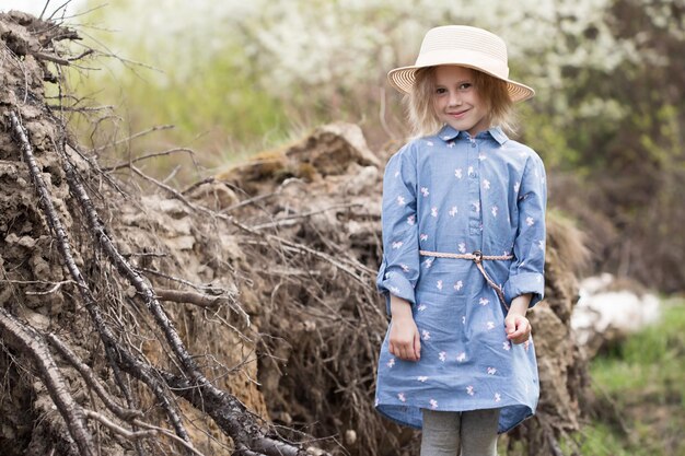 Ritratto di piccola ragazza caucasica di 5 anni in piedi accanto a un albero caduto con radici capovolte nella foresta e sembra dritto