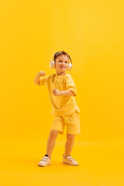 Ritratto di piccolo bambino allegro che ascolta musica in cuffia in posa isolato su sfondo giallo