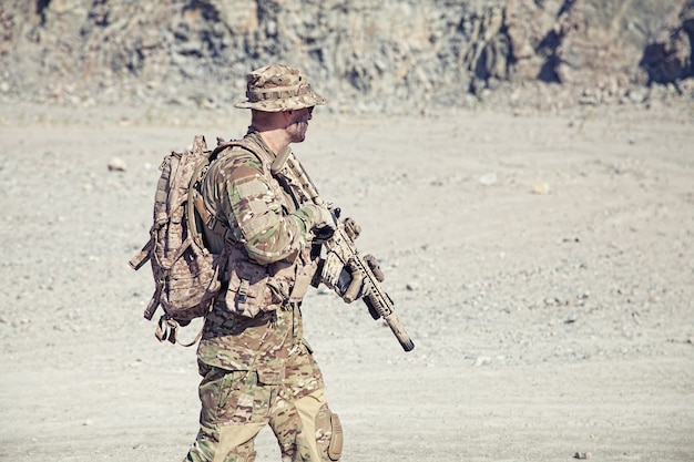 Ritratto di posizione del soldato in uniforme da campo con il fucile nel deserto tra le rocce