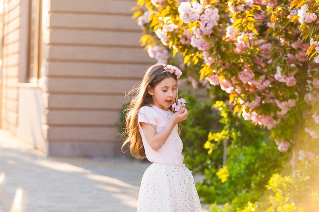 Ritratto di primavera, adorabile bambina con cappello a piedi nel giardino degli alberi in fiore al tramonto