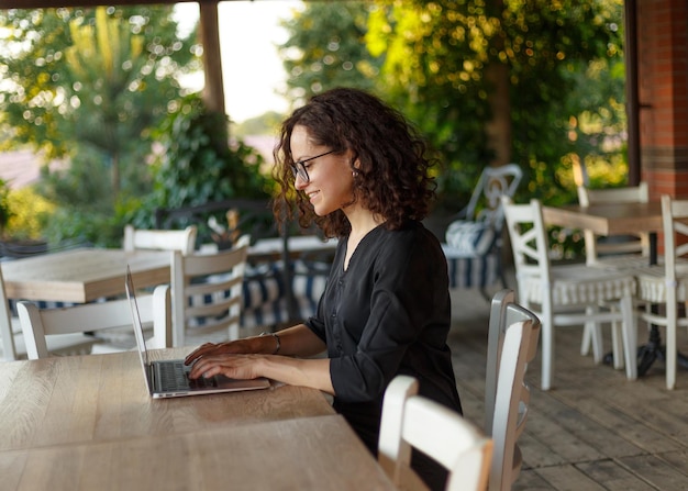 Ritratto di profilo della bella giovane donna seduta al tavolo che digita sul computer portatile sulla terrazza