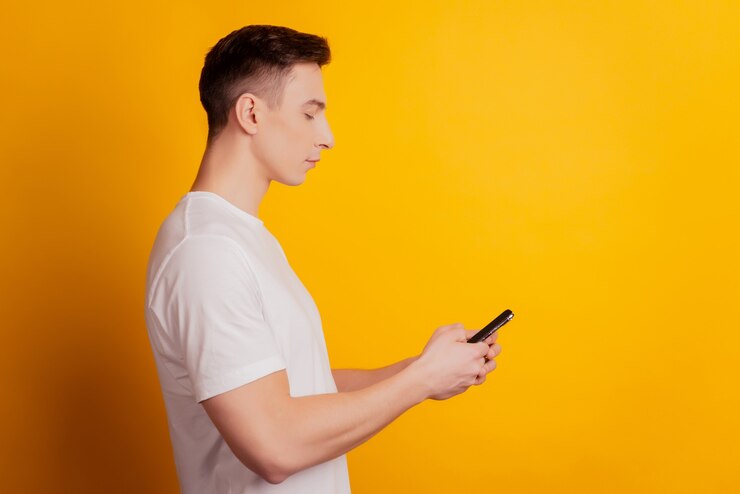 Ritratto di profilo di giovane uomo d'affari affascinante tenere il telefono in chat su sfondo giallo