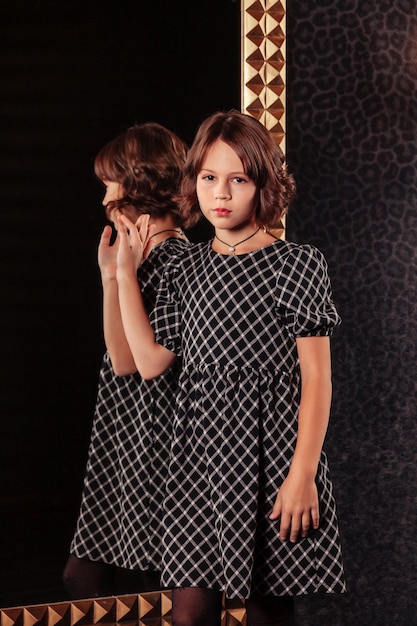 Ritratto di ragazza adolescente piuttosto carina in un vestito elegante allo specchio