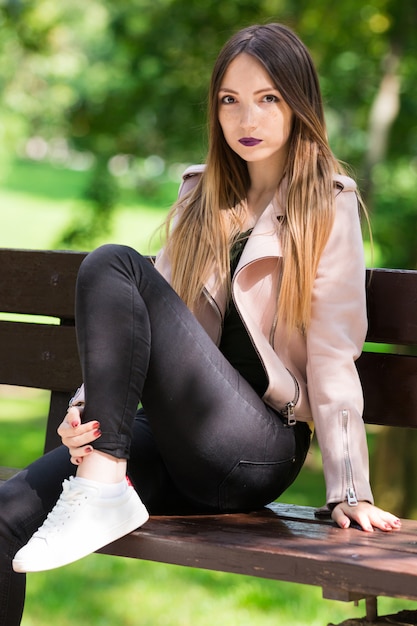 Ritratto di ragazza alla moda sul banco nel parco