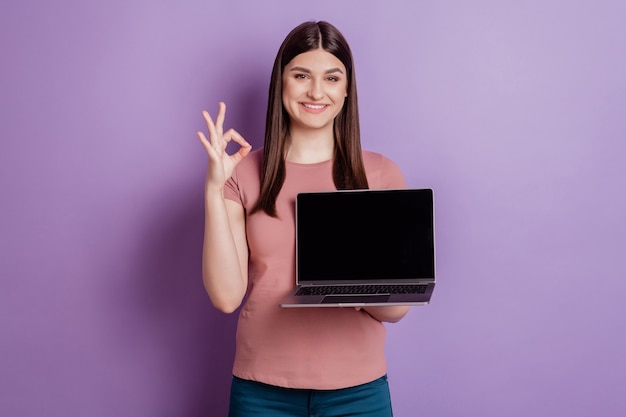 Ritratto di ragazza amichevole felice sorriso positivo mani che tengono il touchscreen del computer portatile mostra okay va bene annuncio isolato su sfondo di colore viola