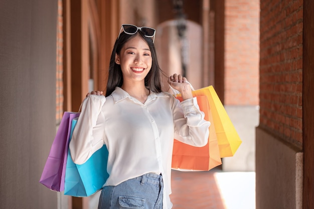 Ritratto di ragazza asiatica eccitata bella ragazza che indossa occhiali da sole sorridenti felici con la tenuta delle borse della spesa godendo nell'espressione rilassata dello shopping, shopping di emozioni positive, concetto di stile di vita.