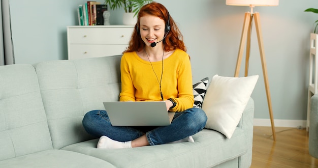 Ritratto di ragazza bella rossa con auricolari utilizzando il computer portatile