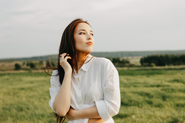 Ritratto di ragazza bella spensierata capelli lunghi in abiti bianchi sul campo al tramonto