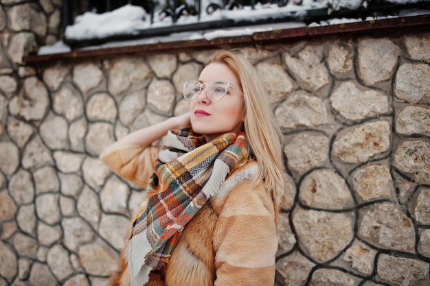 Ritratto di ragazza bionda con gli occhiali, pelliccia rossa e sciarpa al giorno d'inverno.