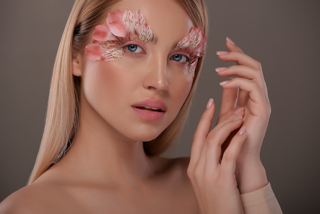 Ritratto di ragazza bionda con trucco creativo piume rosa.