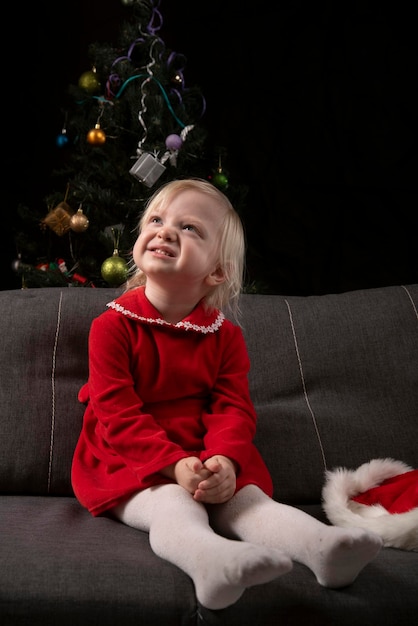 Ritratto di ragazza bionda in abito rosso su sfondo albero di Natale. Bambino in attesa di Natale.