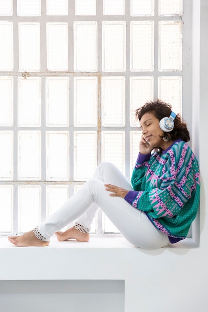 Ritratto di ragazza bruna ascoltando musica seduto sulla finestra. Spazio per il testo.