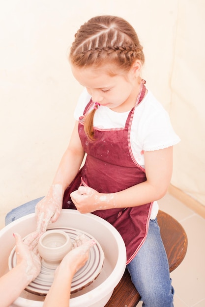 Ritratto di ragazza che cerca di realizzare ceramiche di argilla bianca su un tornio da vasaio