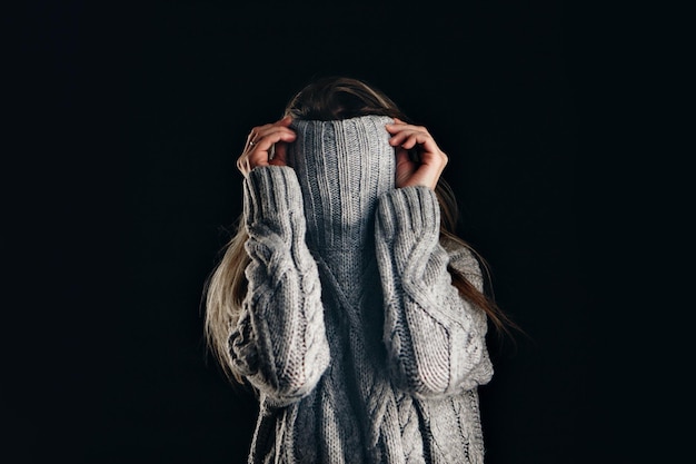 Ritratto di ragazza che tira il suo maglione alla moda sopra la testa divertendosi