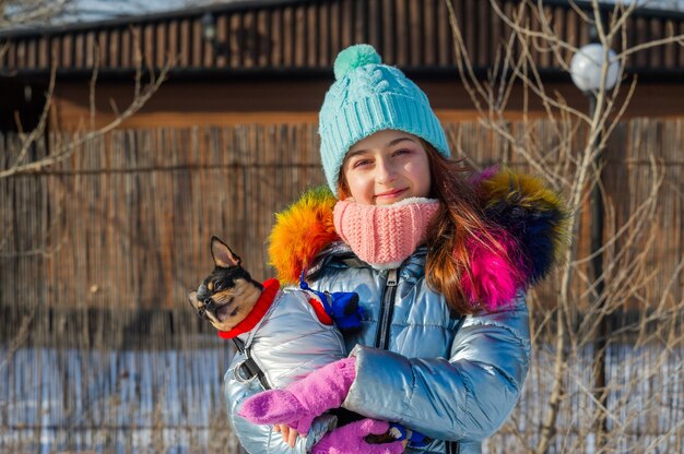 Ritratto di ragazza con giacca e cappello che abbraccia un cane chihuaha nel parco innevato