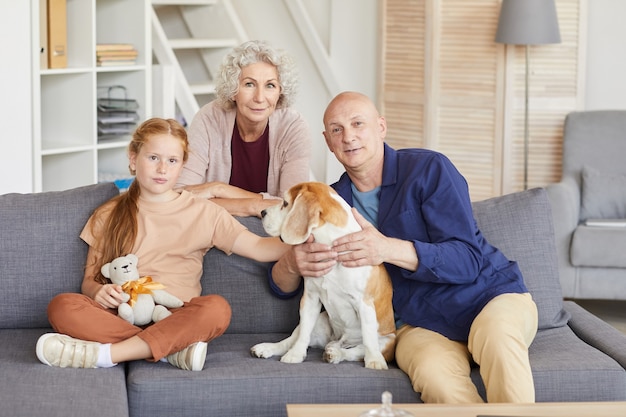 ritratto di ragazza dai capelli rossi con i nonni seduti sul divano e giocare con il cane in casa accogliente