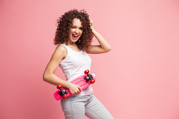 Ritratto di ragazza divertente hipster con longboard rosa su rosa.