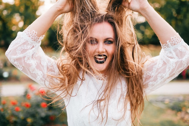 Ritratto di ragazza eccitata con trucco gotico allungando i capelli lunghi con espressione facciale.