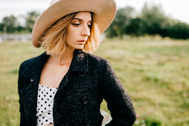 Ritratto di ragazza elegante alla moda capelli corti biondi in cappello in posa nel campo