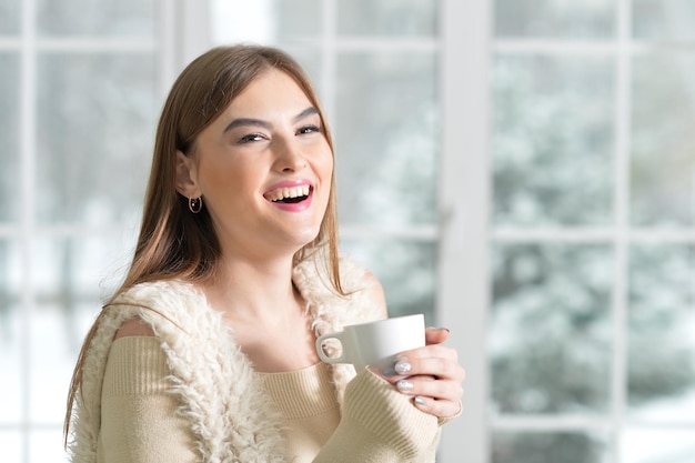 Ritratto di ragazza felice che beve tè vicino alla finestra