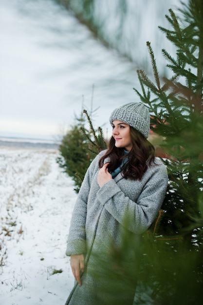 Ritratto di ragazza gentile in cappotto grigio e cappello contro l'albero di Capodanno all'aperto.