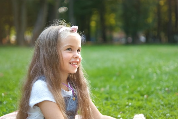 Ritratto di ragazza graziosa del bambino in seduta nel parco estivo sorridendo felicemente.