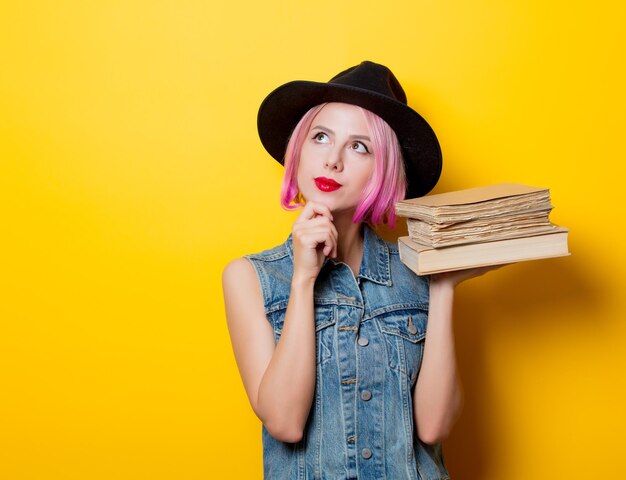 Ritratto di ragazza hipster stile giovane con acconciatura rosa con libri su sfondo giallo