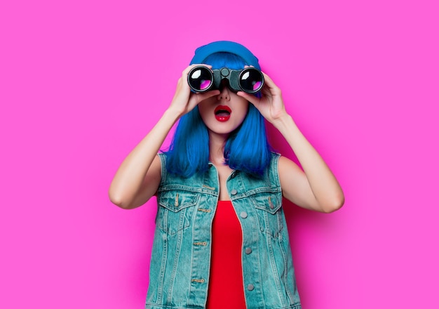 Ritratto di ragazza hipster stile giovane con capelli blu e binocolo su sfondo rosa