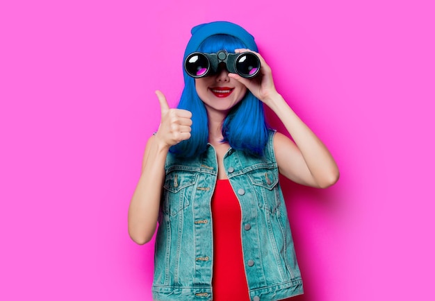 Ritratto di ragazza hipster stile giovane con capelli blu e binocolo su sfondo rosa