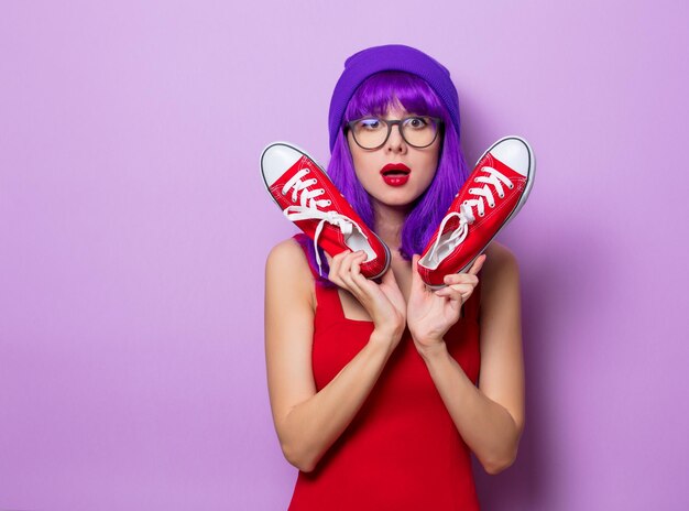 Ritratto di ragazza hipster stile giovane con capelli blu e scarpe da ginnastica rosse su sfondo di colore viola