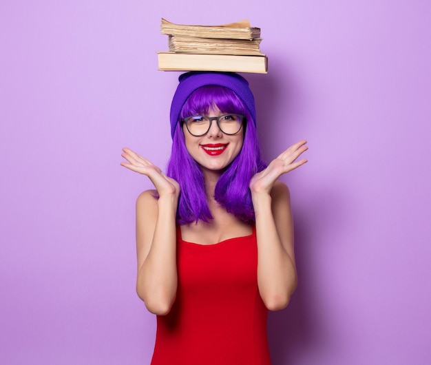 Ritratto di ragazza hipster stile giovane con capelli viola e libri su sfondo di colore viola