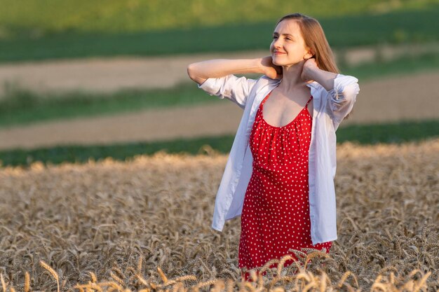 Ritratto di ragazza in campo in raggi del sole al tramonto Giovane donna in prendisole rosso ammira la raccolta del pane
