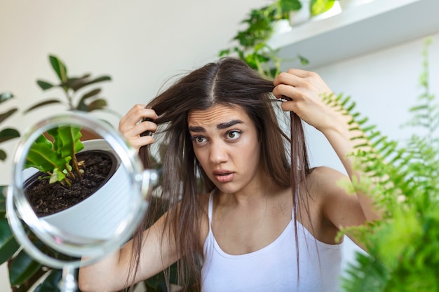 Ritratto di ragazza nervosa sconvolta che si passa le dita tra i capelli e pensa alla forfora e alla perdita di capelli con emozioni tristi. Concetto di problema di perdita dei capelli