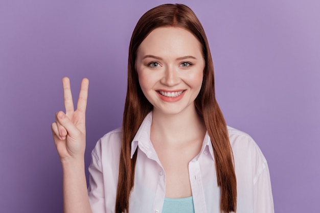 Ritratto di ragazza piuttosto positiva che gesturing simbolo di pace v-sign isolato su sfondo viola