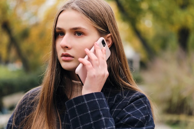 Ritratto di ragazza seria attraente che parla sul cellulare all'aperto