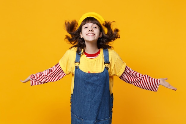 Ritratto di ragazza sorridente adolescente in berretto francese che salta con i capelli fluenti che diffondono le mani isolate su sfondo giallo muro in studio. Persone sincere emozioni concetto di stile di vita. Mock up spazio di copia.