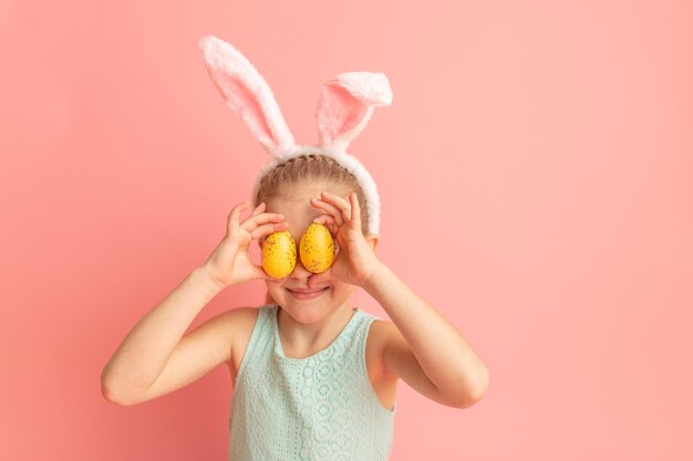 Ritratto di ragazza sorridente carina con orecchie da coniglio e uova di Pasqua gialle chiude gli occhi con i testicoli