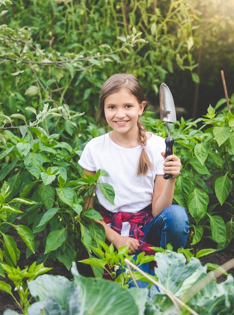 Ritratto di ragazza sorridente carina in posa con la cazzuola al giardino fiorito