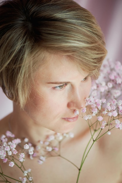 Ritratto di ragazza su sfondo rosa con fiori Tenerezza e femminilità La sfera della bellezza e della salute delle donne Taglio corto capelli biondi