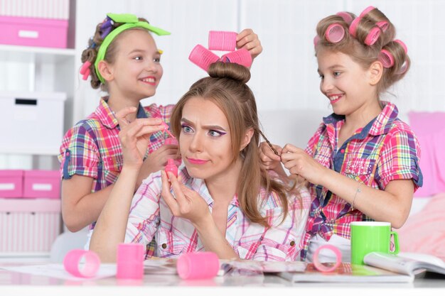 Ritratto di ragazze gemelle con madre in bigodini facendo acconciatura