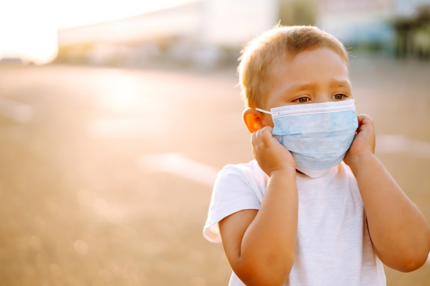 Ritratto di ragazzino con maschera medica che guarda la telecamera in città