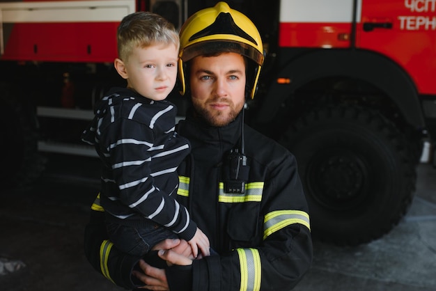 Ritratto di ragazzino salvato con uomo vigile del fuoco in piedi vicino al camion dei pompieri Vigile del fuoco in operazione antincendio