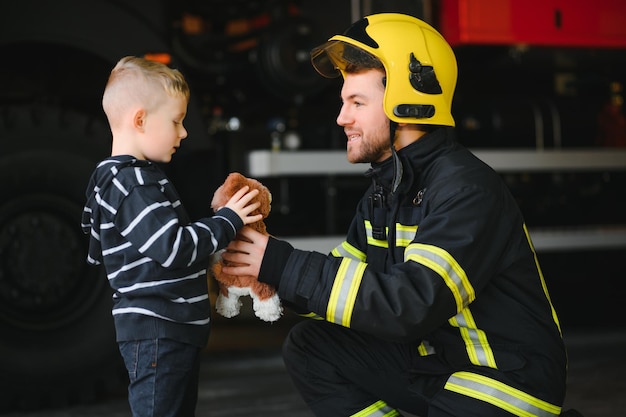 Ritratto di ragazzino salvato con uomo vigile del fuoco in piedi vicino al camion dei pompieri Vigile del fuoco in operazione antincendio