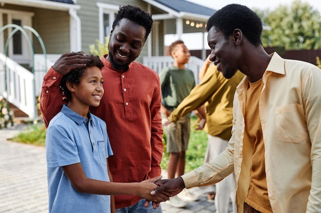 Ritratto di ragazzo afroamericano sorridente che stringe la mano al membro della famiglia durante la riunione per l'estate