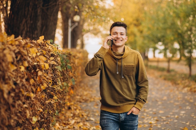 Ritratto di ragazzo bello e felice, sorridente e parlando al telefono nel parco in autunno