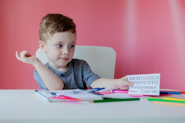 Ritratto di ragazzo carino a casa che fa i compiti Piccolo bambino concentrato che scrive con una matita colorata all'interno Scuola elementare e istruzione Bambino che impara a scrivere lettere e numeri