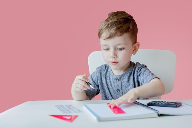 Ritratto di ragazzo carino a casa che fa i compiti Piccolo bambino concentrato che scrive con una matita colorata all'interno Scuola elementare e istruzione Bambino che impara a scrivere lettere e numeri