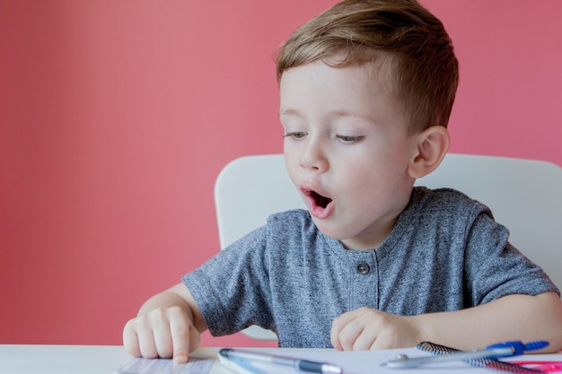 Ritratto di ragazzo carino a casa che fa i compiti Piccolo bambino concentrato che scrive con una matita colorata all'interno Scuola elementare e istruzione Bambino che impara a scrivere lettere e numeri