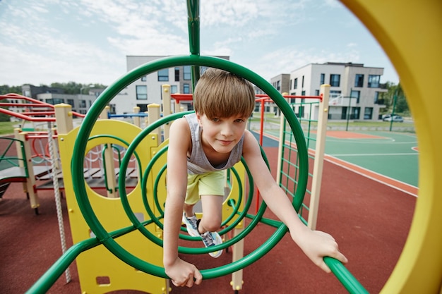 Ritratto di ragazzo che gioca nella palestra della giungla su un parco giochi colorato e guardando lo spazio della copia della fotocamera