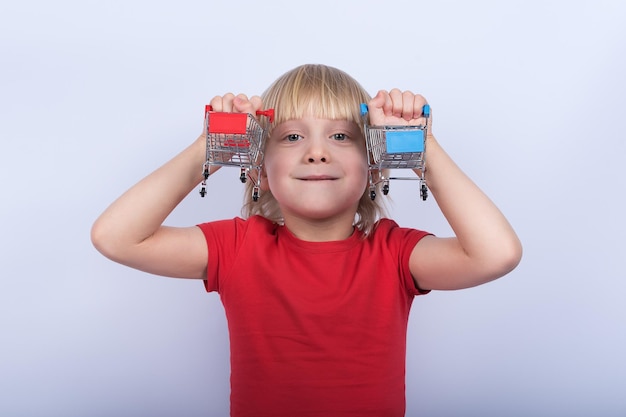 Ritratto di ragazzo dai capelli chiari con carrello giocattolo su sfondo bianco Concetto di shopping per i bambini